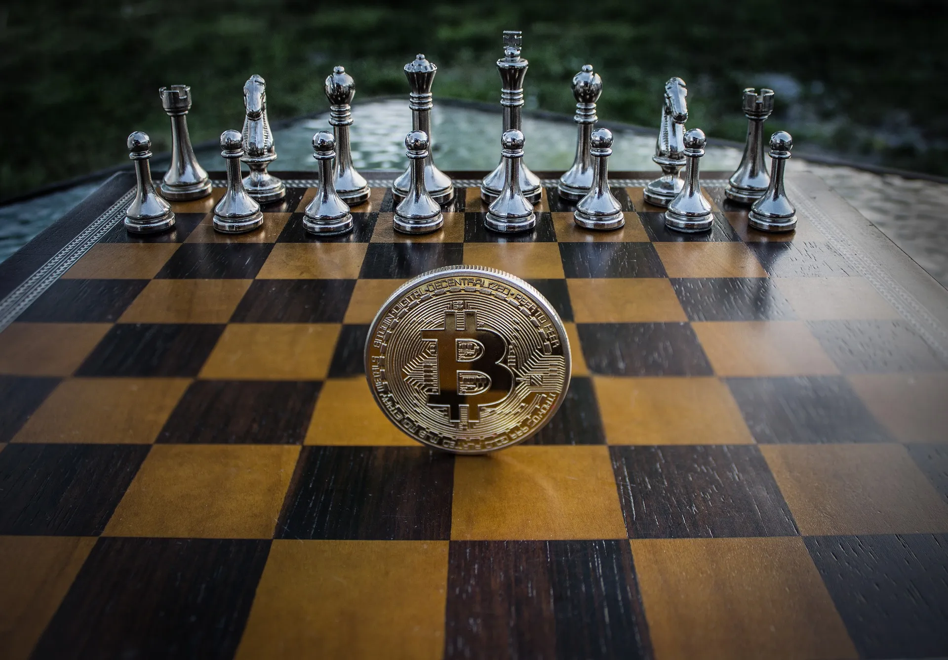 Chess board with metallic chess pieces set up and a large cryptocurrency coin standing upright in front, blurred green background